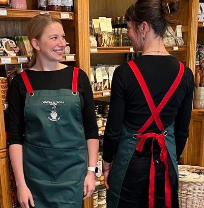 Two staff members wearing the green Valvona & Crolla apron with red straps in the shop