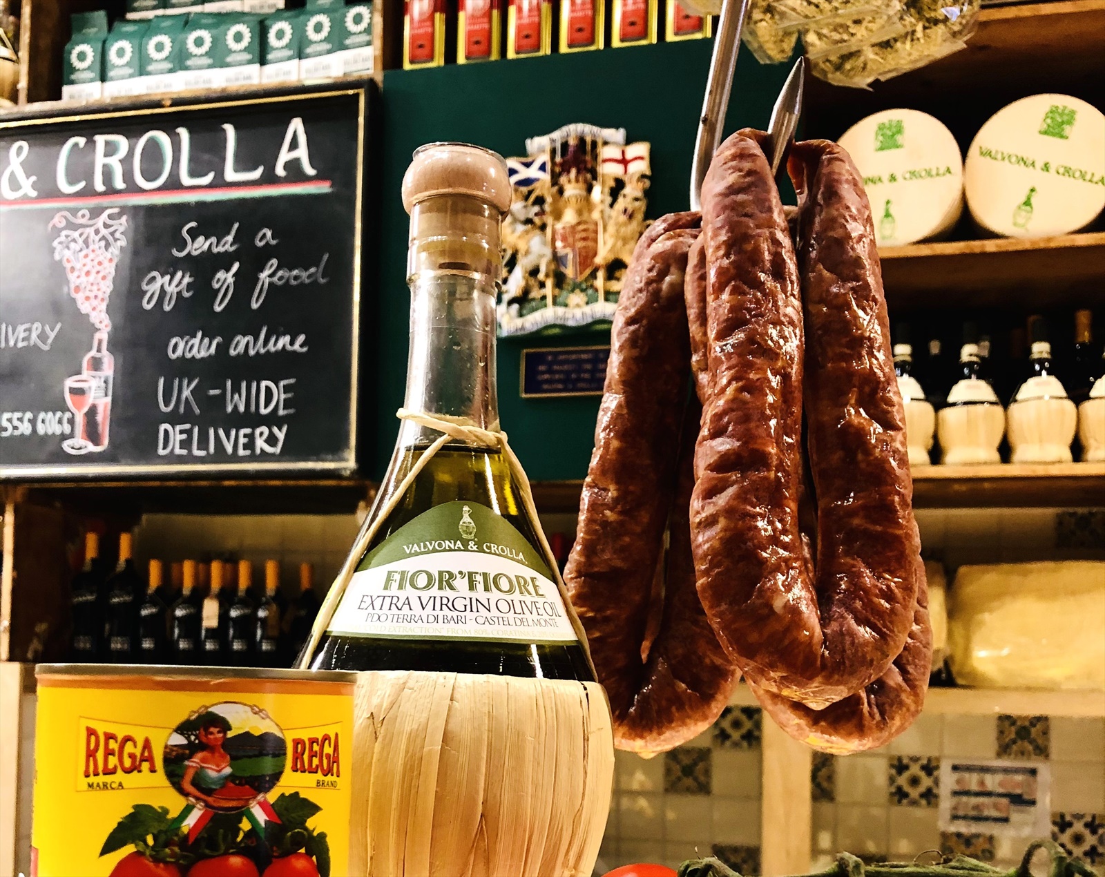 Inside the deli — Fonteluna sausages hanging over the counter, Fior&rsquo; Fiore olive oil, V&C cheese wheels and the UK-wide delivery chalkboard