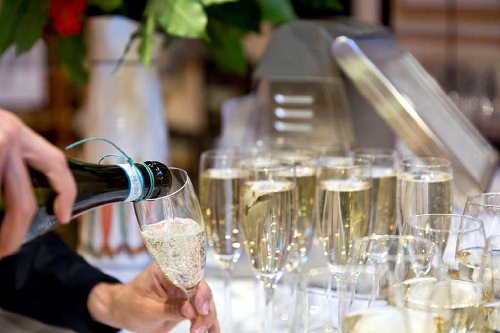 Sparkling wine being poured into a flute among rows of filled glasses at a festival tasting