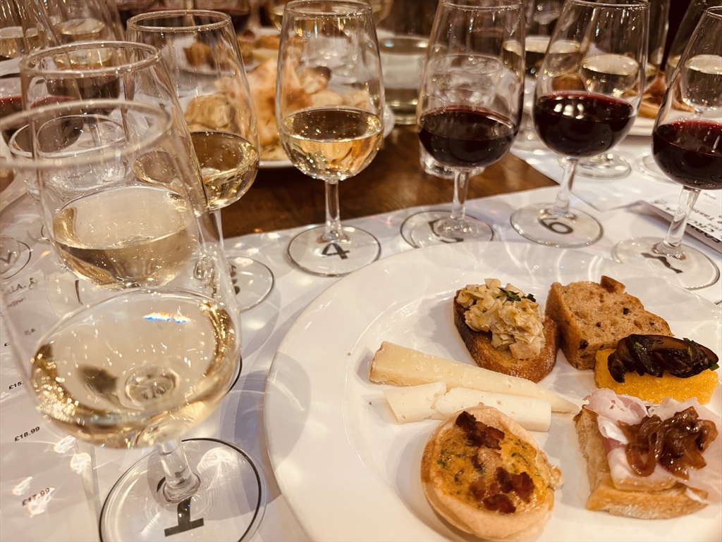 Numbered tasting glasses of white and red wine beside a plate of crostini and cheese